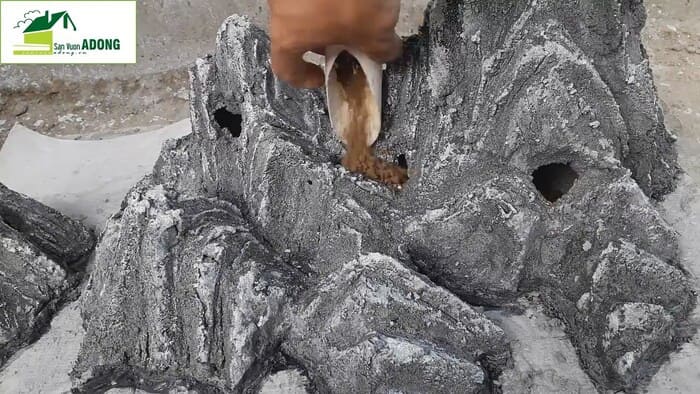 Dùng thìa hoặc cốc đổ đất vào các hốc đá của hòn non bộ